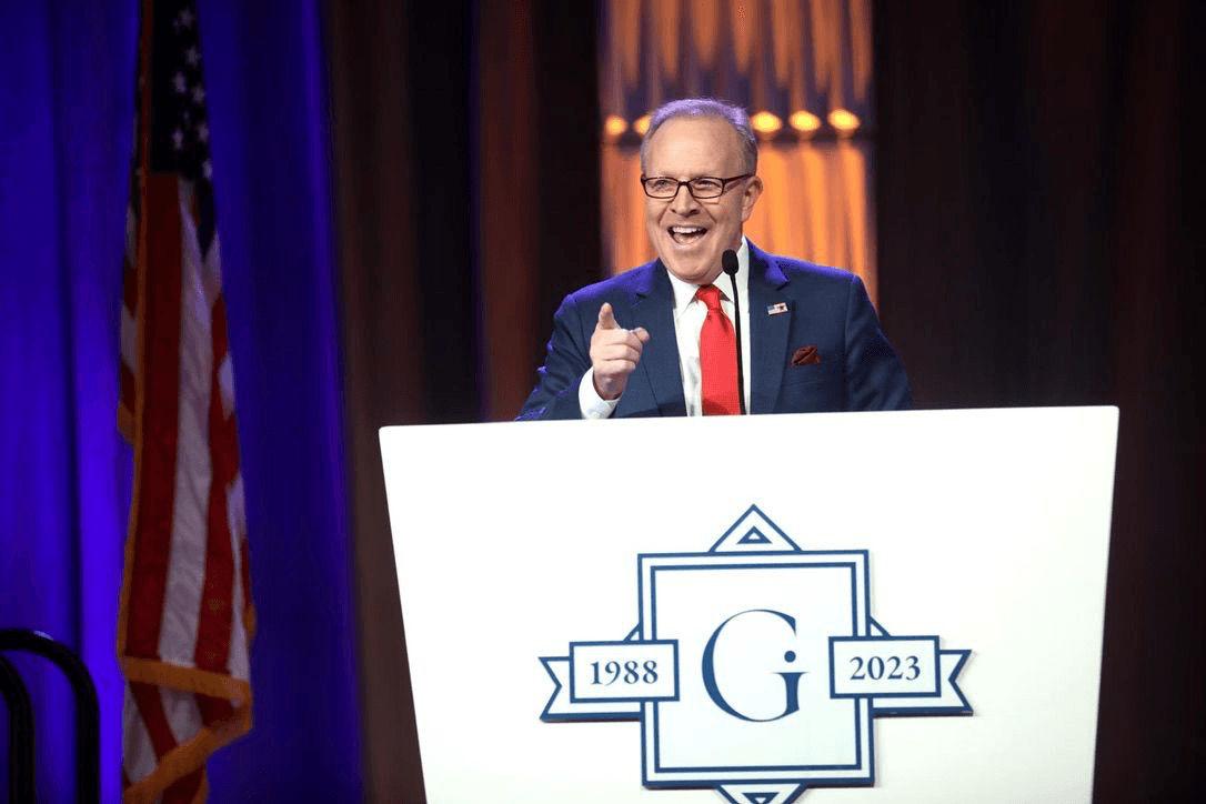 Kent Emmons speaking at a podium beside an American flag